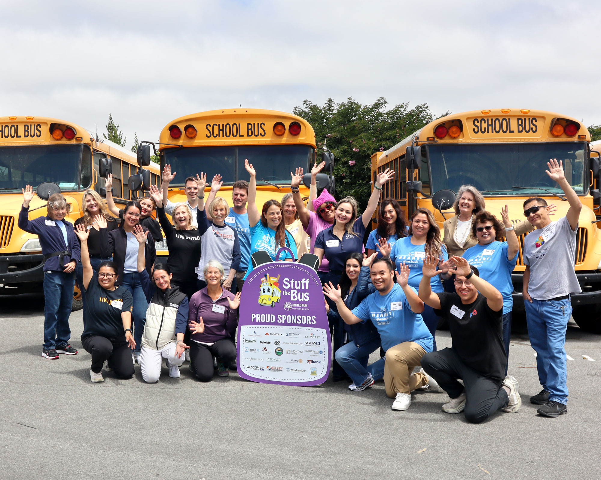 Group of volunteers in front of school buses with Stuff the Bus sign